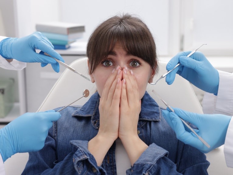 dental patient anxiety: Anxious dental patient covering her mouth while multiple dental instruments approach her