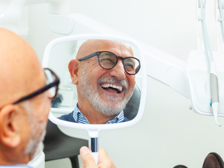 happy patient dental technology: Smiling older dental patient looking at his reflection in a hand mirror during a dental appointment