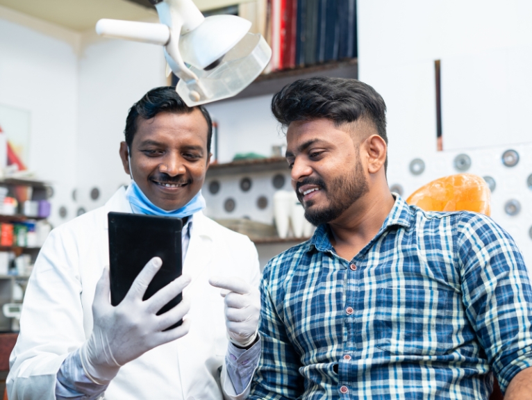 AI in dentistry National Dentists’ Day: Dentist showing a patient dental images on a tablet in a modern surgery