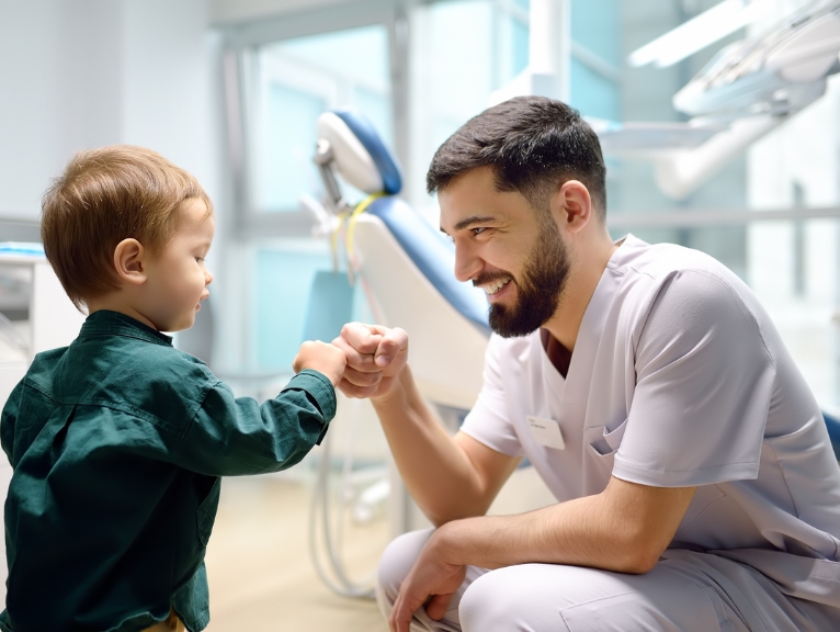Dental Design: Dentist crouching to greet young child patient with a friendly fist bump in a treatment room.