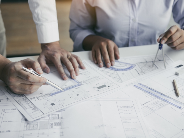 Dental Equipment Design: Designers reviewing detailed architectural plans with compass and ruler on a drafting table.