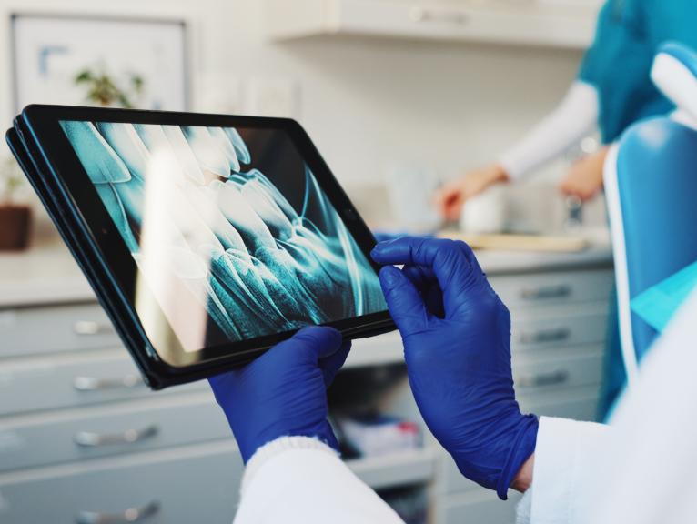 Dental practice efficiency Close-up of a dental professional in blue gloves holding a tablet displaying a digital dental X-ray.