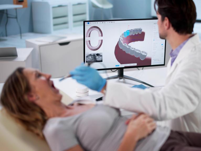 Dental workflow efficiency A dentist reviews a 3D digital scan of a patient's teeth on a monitor while the patient reclines in the treatment chair.