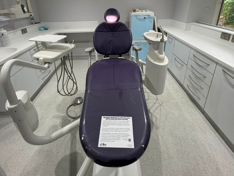 Dental practice fit-out company UK: A freshly fitted dental surgery room featuring a purple dental chair with an overhead light, dental equipment, and white cabinetry.